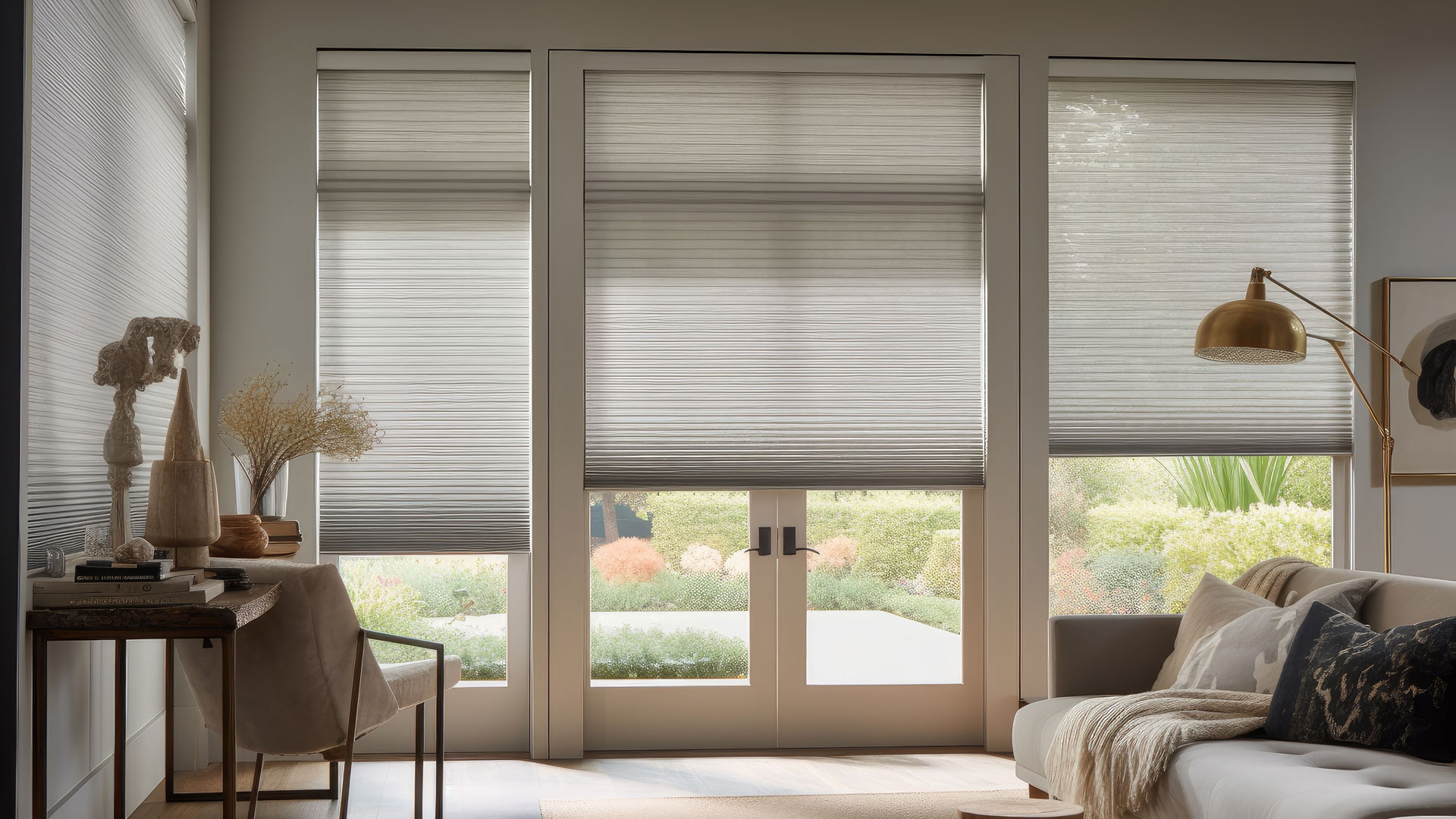 Modern living room with large windows and glass doors covered by light-colored pleated blinds, neutral-toned furniture, a gold floor lamp, and views of a lush garden—perfect inspiration for your next home remodeling Charlotte NC project.